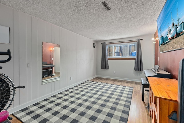 office area with a textured ceiling, light wood-type flooring, and wood walls