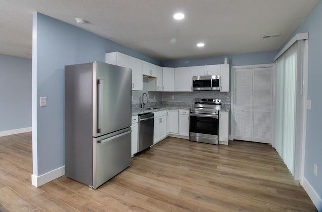 kitchen featuring sink, light hardwood / wood-style flooring, decorative backsplash, appliances with stainless steel finishes, and white cabinetry