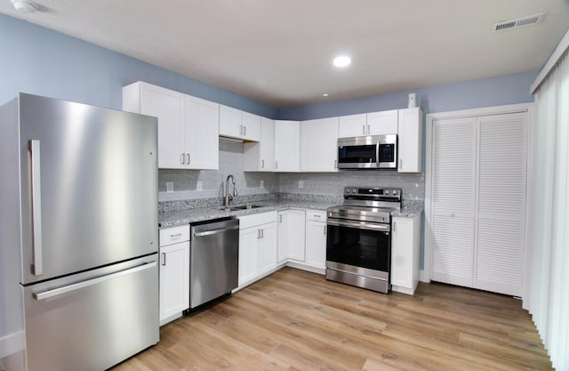 kitchen featuring decorative backsplash, appliances with stainless steel finishes, light stone counters, sink, and white cabinetry