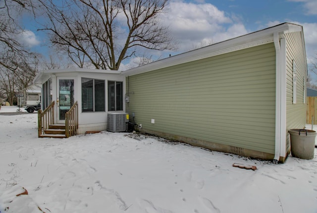 snow covered rear of property with central AC and a sunroom