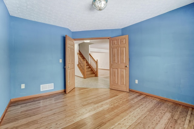 spare room with a textured ceiling and light hardwood / wood-style flooring