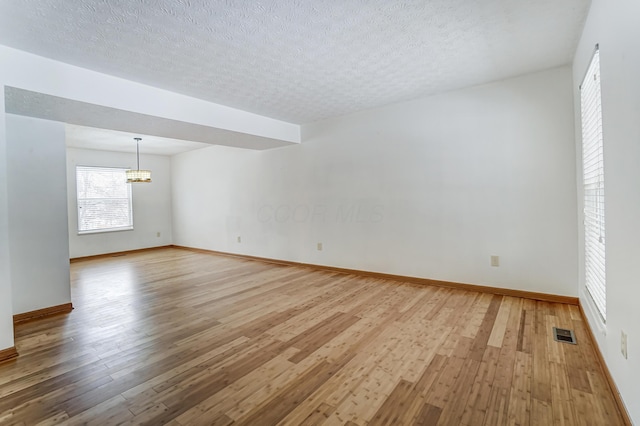 spare room with a textured ceiling, light hardwood / wood-style floors, and an inviting chandelier