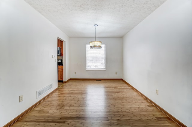 unfurnished dining area featuring a chandelier, a textured ceiling, and light hardwood / wood-style flooring