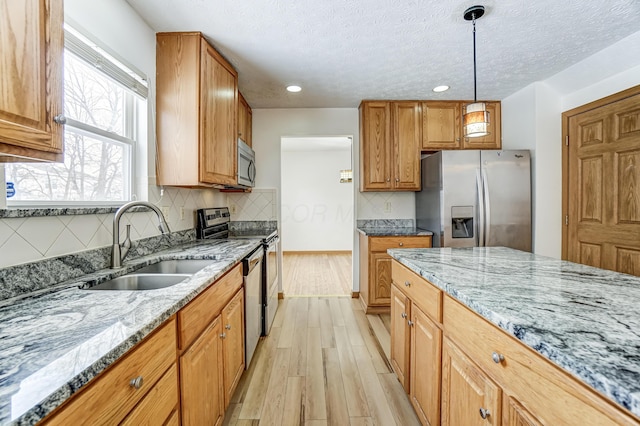 kitchen with light wood-type flooring, light stone counters, stainless steel appliances, sink, and pendant lighting