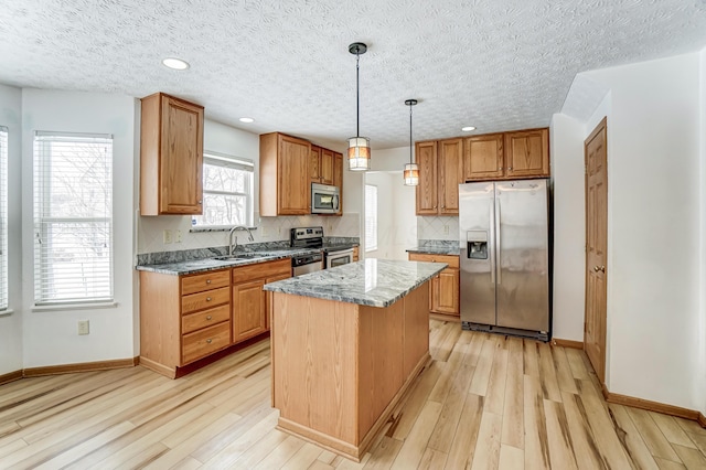 kitchen with light stone countertops, sink, a center island, decorative light fixtures, and appliances with stainless steel finishes