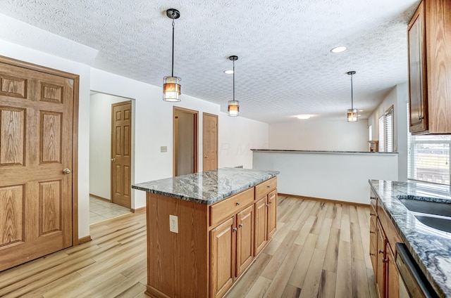 kitchen featuring stainless steel dishwasher, a textured ceiling, dark stone countertops, a center island, and hanging light fixtures