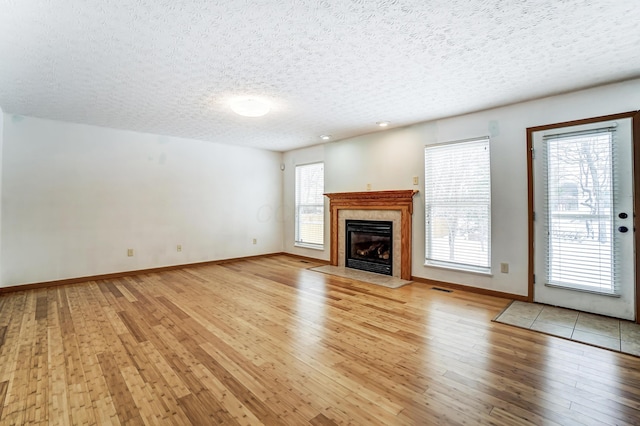 unfurnished living room featuring a textured ceiling, light hardwood / wood-style floors, and a tiled fireplace