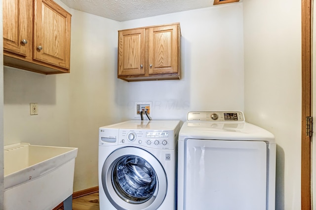 laundry room featuring cabinets, a textured ceiling, washing machine and dryer, and sink