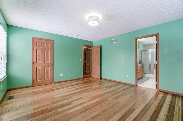 unfurnished bedroom with a textured ceiling, ensuite bathroom, and light hardwood / wood-style floors