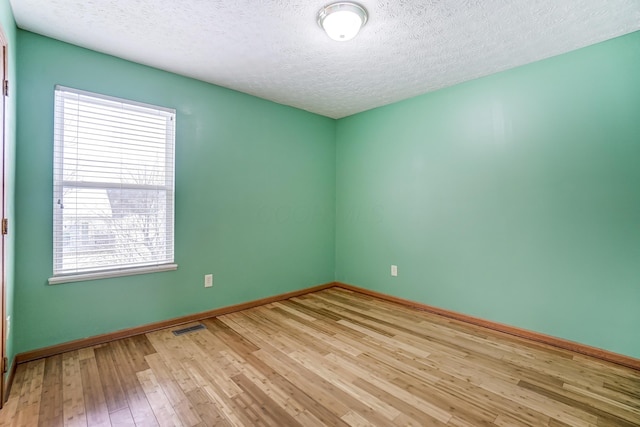 spare room featuring light wood-type flooring and a textured ceiling