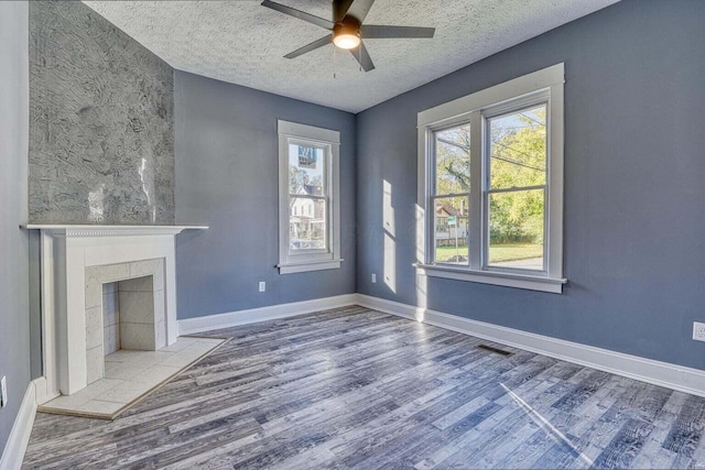 unfurnished living room featuring a tile fireplace, a textured ceiling, ceiling fan, and hardwood / wood-style flooring