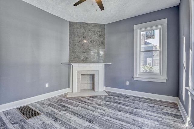 unfurnished living room with a textured ceiling, ceiling fan, hardwood / wood-style floors, and a fireplace