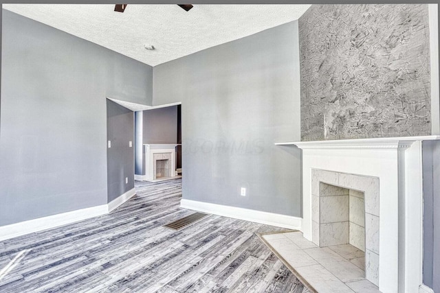 unfurnished living room with a fireplace, a textured ceiling, ceiling fan, and light hardwood / wood-style flooring