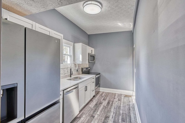 kitchen with a textured ceiling, tasteful backsplash, white cabinetry, appliances with stainless steel finishes, and sink