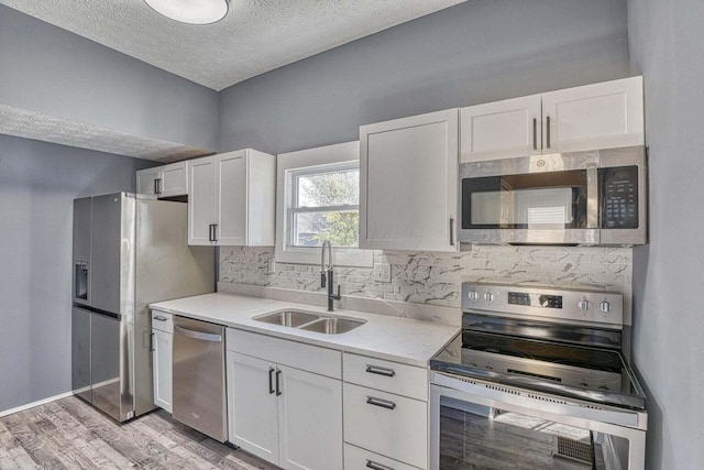 kitchen featuring a textured ceiling, stainless steel appliances, light wood-type flooring, white cabinets, and sink