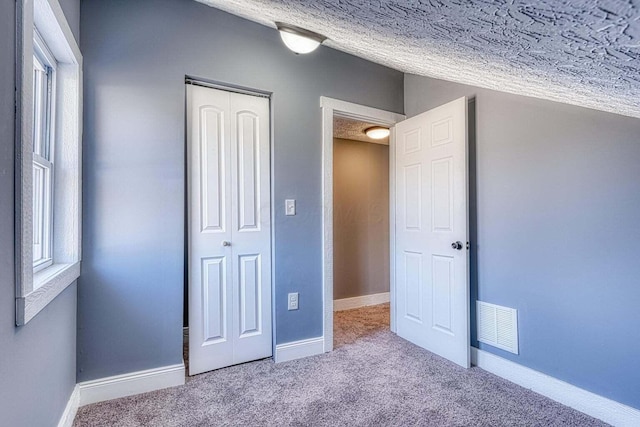 unfurnished bedroom with a textured ceiling, a closet, light carpet, and multiple windows