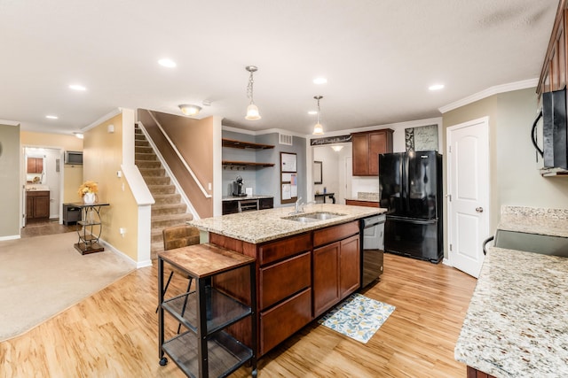 kitchen featuring sink, hanging light fixtures, light stone counters, black appliances, and a center island with sink