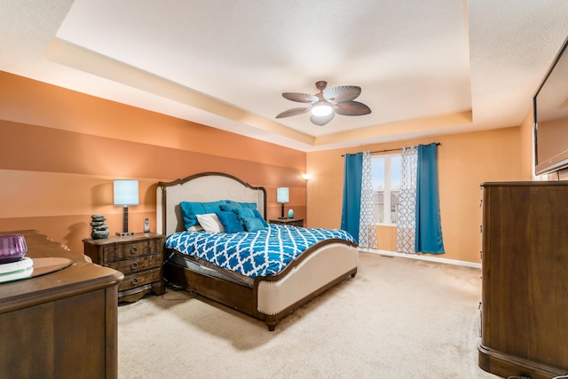 carpeted bedroom with a raised ceiling and ceiling fan