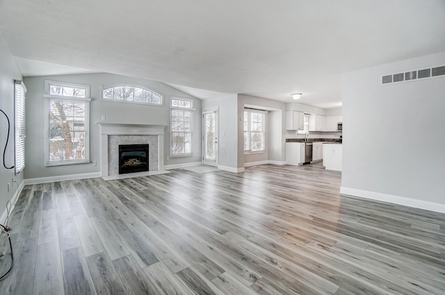 unfurnished living room with a tile fireplace, light hardwood / wood-style flooring, and lofted ceiling