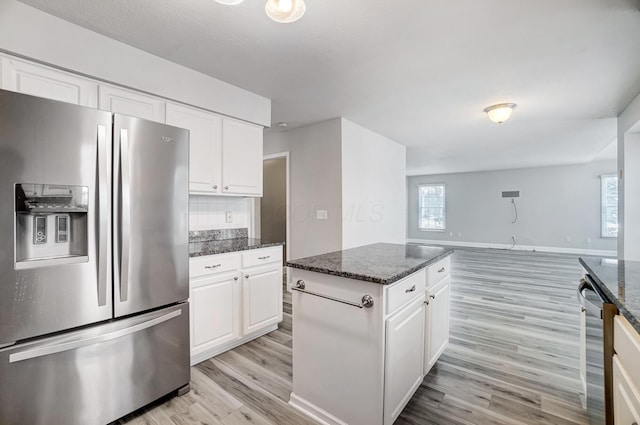 kitchen with tasteful backsplash, dark stone counters, stainless steel appliances, white cabinets, and light hardwood / wood-style floors