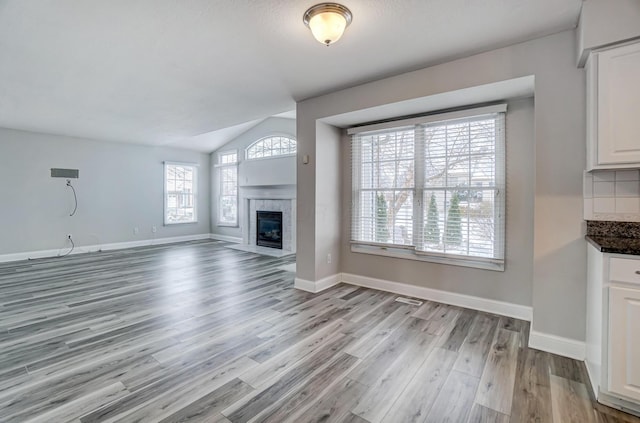 unfurnished living room with light hardwood / wood-style floors, vaulted ceiling, a wealth of natural light, and a tiled fireplace