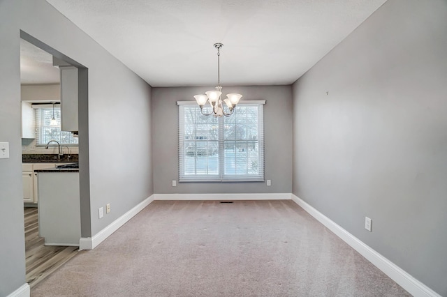 unfurnished dining area with light colored carpet, sink, and a chandelier