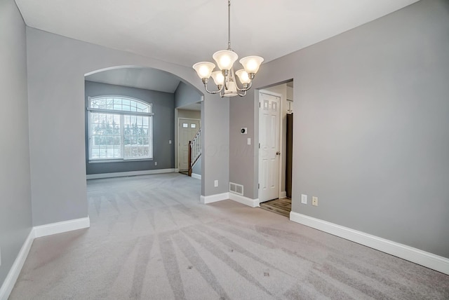 spare room featuring light carpet and an inviting chandelier