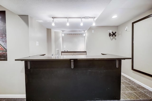 bar featuring dark tile patterned floors, rail lighting, and a textured ceiling