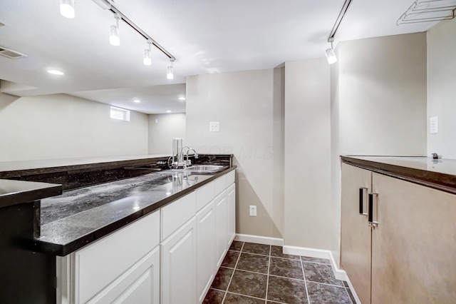 kitchen with dark tile patterned floors, sink, white cabinets, and dark stone counters