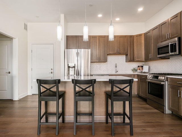 kitchen with a center island, appliances with stainless steel finishes, hanging light fixtures, a kitchen breakfast bar, and dark wood-type flooring