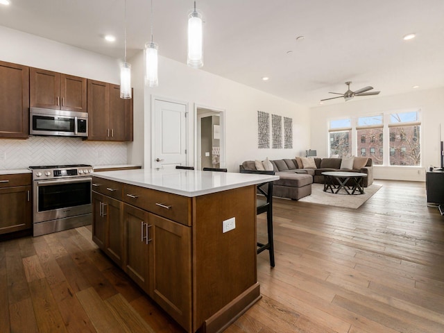 kitchen featuring pendant lighting, a kitchen island, stainless steel appliances, hardwood / wood-style flooring, and a breakfast bar