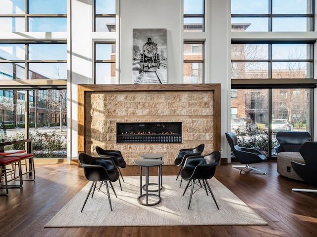 living area featuring a healthy amount of sunlight, hardwood / wood-style flooring, a towering ceiling, and a stone fireplace