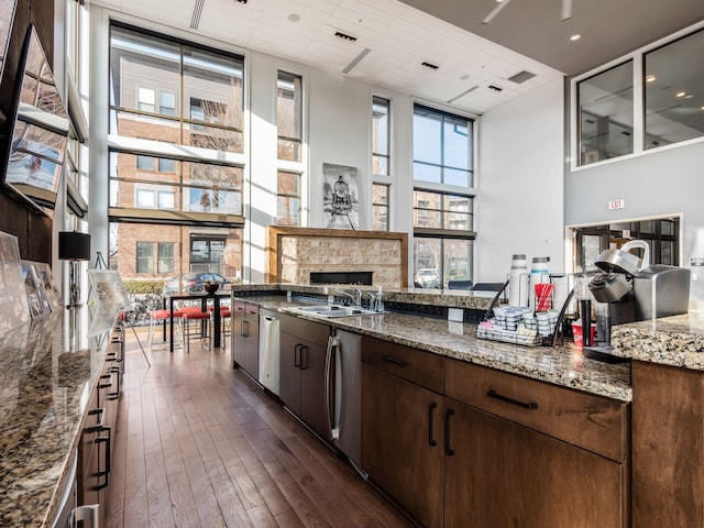 kitchen featuring a high ceiling, dark wood-type flooring, a fireplace, sink, and stainless steel dishwasher