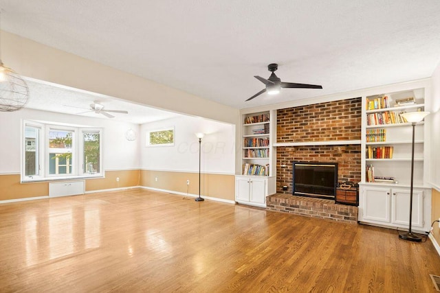 unfurnished living room with ceiling fan, a fireplace, built in features, and light wood-type flooring