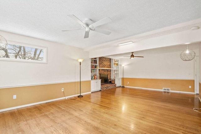 unfurnished living room featuring a fireplace, built in shelves, a textured ceiling, and wood-type flooring