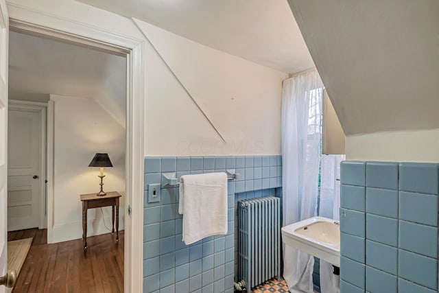 bathroom featuring hardwood / wood-style floors, vaulted ceiling, radiator heating unit, and tile walls