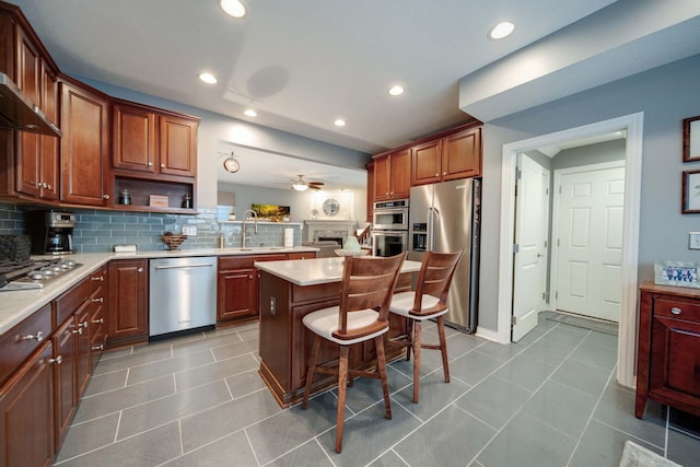 kitchen with a breakfast bar area, tasteful backsplash, a center island, appliances with stainless steel finishes, and ceiling fan