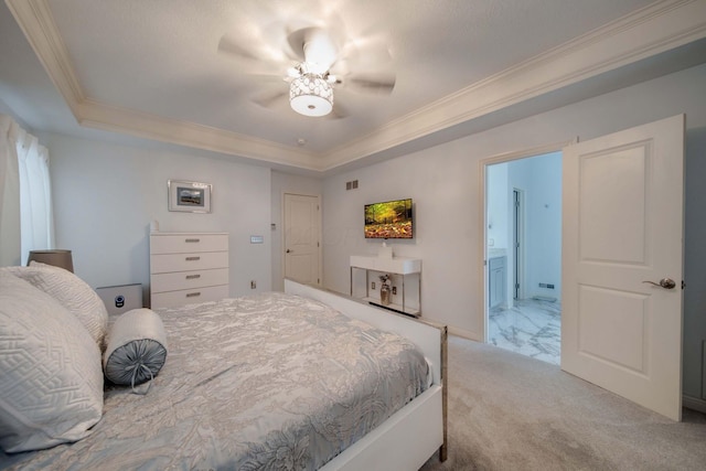 bedroom featuring ceiling fan, ensuite bathroom, a tray ceiling, ornamental molding, and light colored carpet