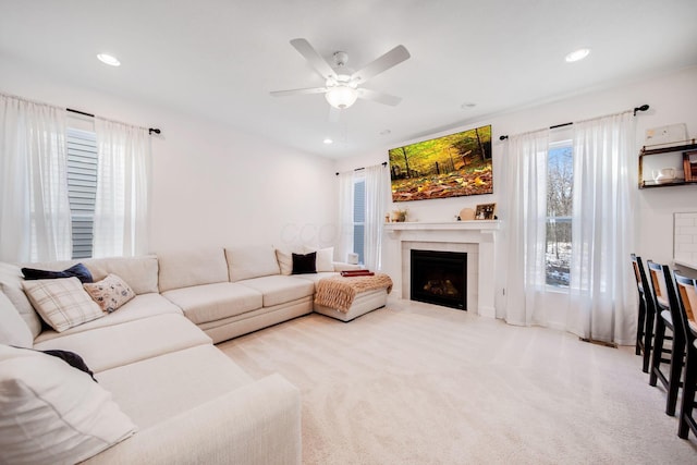 living room with a tiled fireplace, light colored carpet, and ceiling fan