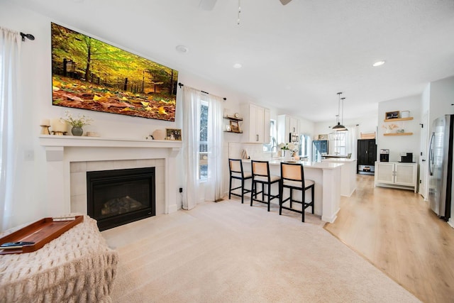 living room with ceiling fan, a tiled fireplace, and light wood-type flooring