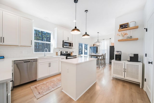 kitchen with white cabinetry, sink, stainless steel appliances, and hanging light fixtures