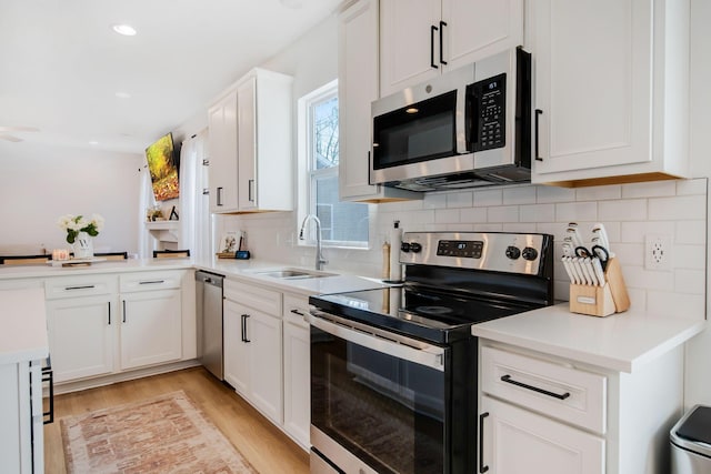 kitchen with appliances with stainless steel finishes, light hardwood / wood-style floors, sink, and white cabinets