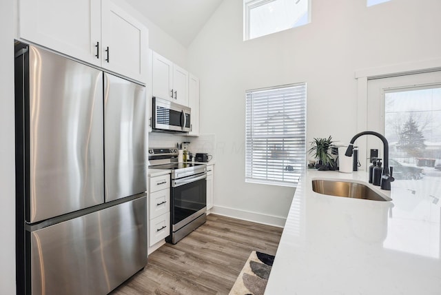 kitchen with tasteful backsplash, sink, white cabinetry, light hardwood / wood-style flooring, and stainless steel appliances