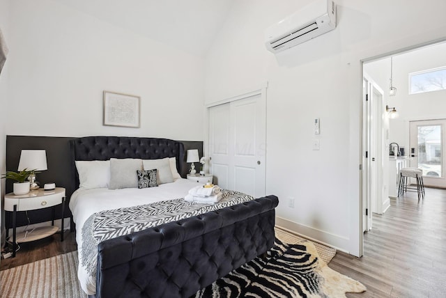 bedroom with high vaulted ceiling, an AC wall unit, a closet, and wood-type flooring