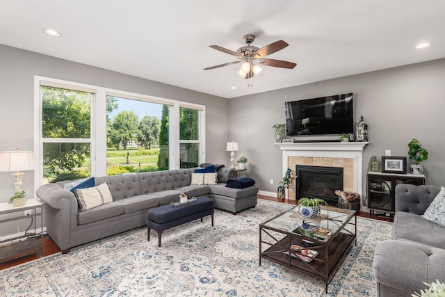 living room featuring a tile fireplace, ceiling fan, and light hardwood / wood-style flooring