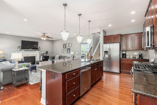 kitchen with appliances with stainless steel finishes, tasteful backsplash, sink, pendant lighting, and a center island with sink