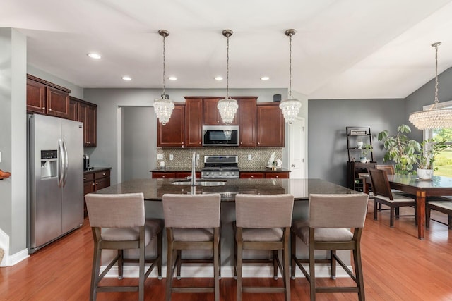 kitchen with hanging light fixtures, stainless steel appliances, and a kitchen island with sink