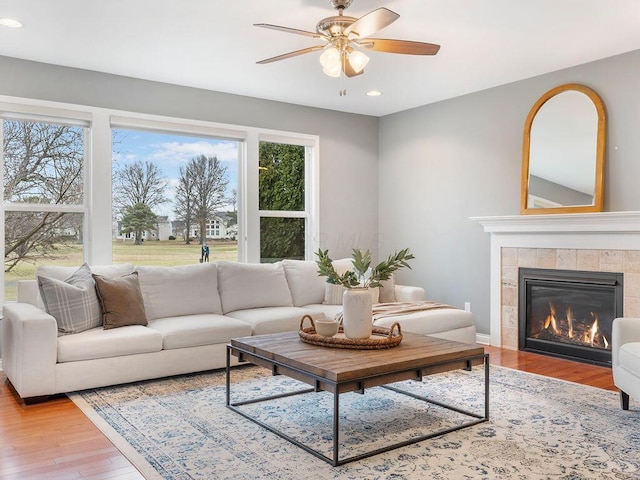 living room featuring a tile fireplace, ceiling fan, and light hardwood / wood-style floors