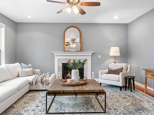 living room with hardwood / wood-style flooring, ceiling fan, and a tiled fireplace