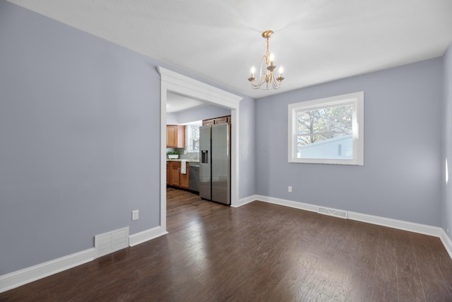 empty room with dark wood-type flooring and a chandelier